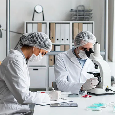 Due addetti al settore chimico con camice, guanti, cuffie e microscopio