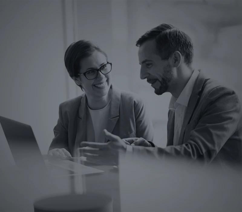 due persone sedute alla scrivania e un computer davanti si confrontano e sorridono