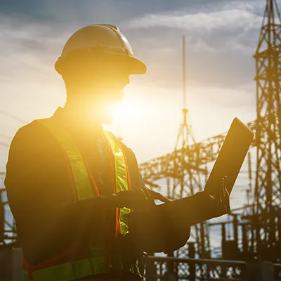 Immagine copertina corso online. Lavoratore in controluce con in mano un pc. Immagine suggestiva in cantiere