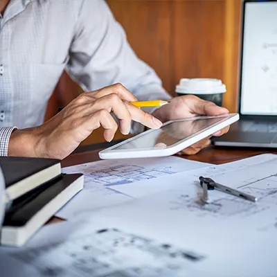 Immagine copertina corso online. BIM Manager alla scrivania lavora con tablet e planimetrie di edifici